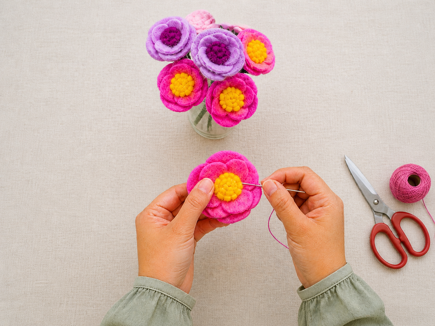 Close-up of hands crafting a felt flower with soft wool textures visible